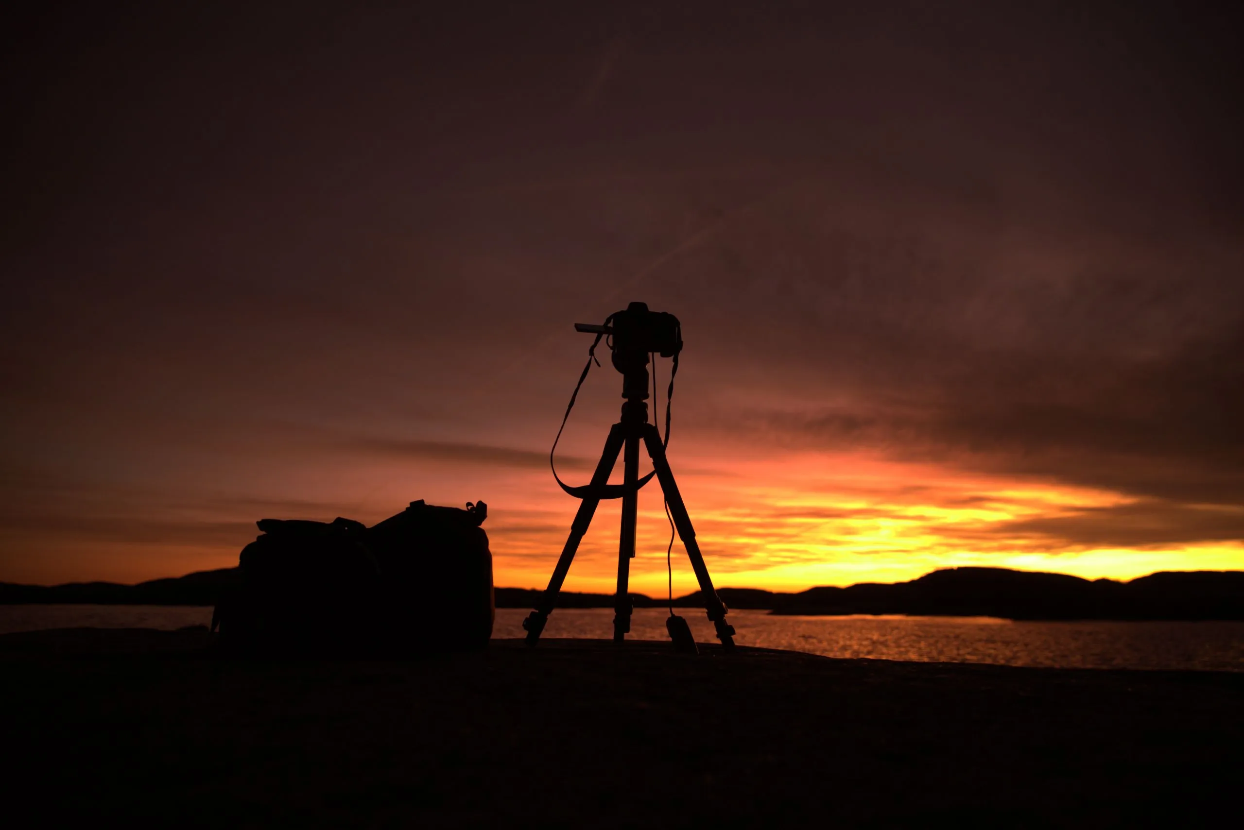 Fotograf ved stativ i silhuett mot en gyllen solnedgang over skjærgården på Sørlandet